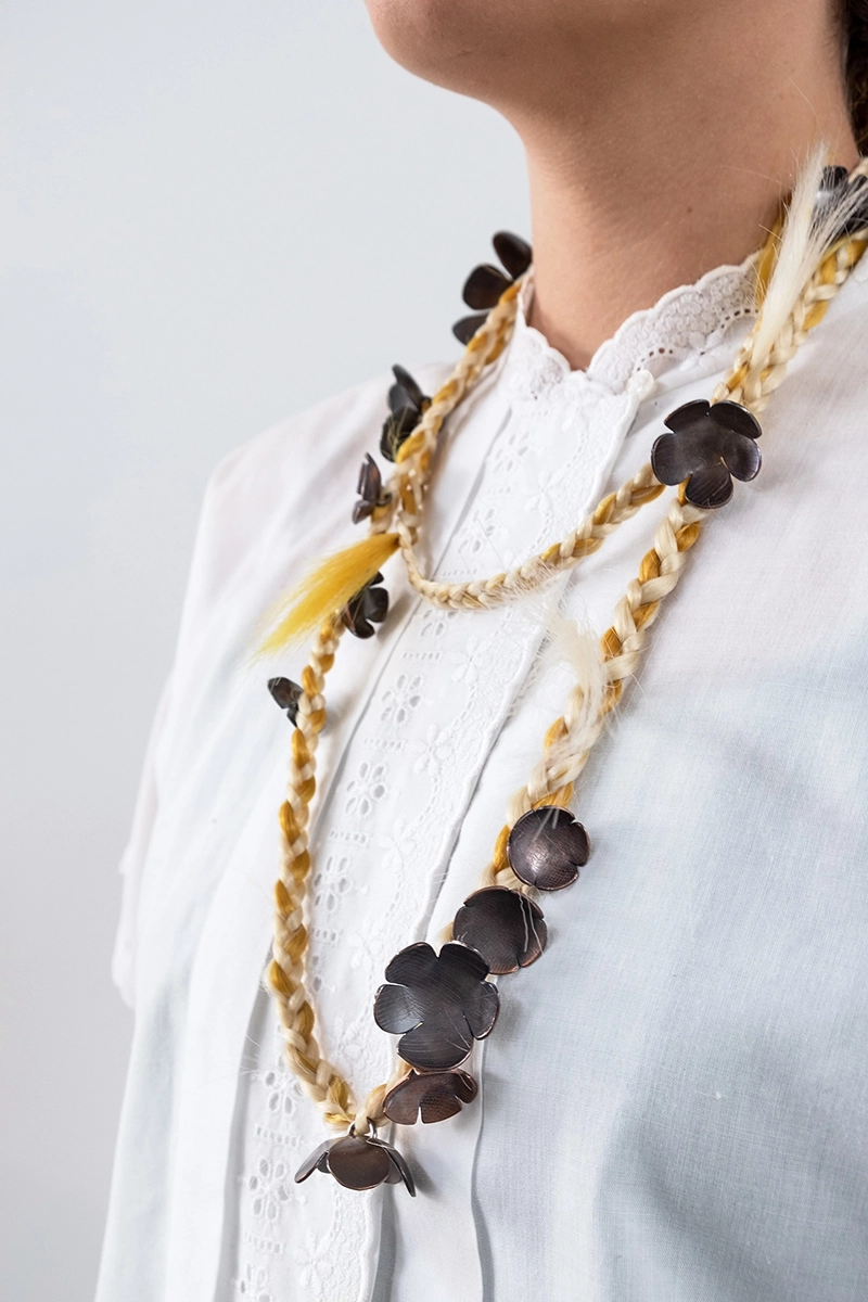 a handcrafted necklace of steel flowers on braided cord is worn by a model in a white shirt